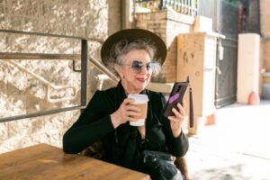 Chic senior woman with coffee and smartphone, indulging in leisure outdoors.